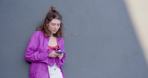 the girl leans against the wall and holds the phone in her hands