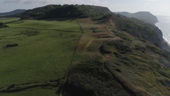 Golden cap and Charmouth beach cliffs are revealed with an aerial track from inland to out to sea lo