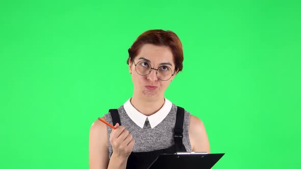 Portrait of Funny Girl in Round Glasses Is Angrily Writing Plans at Black Folder with Pencil. Green