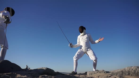 A man and woman fencing on the beach.