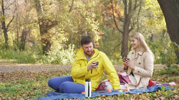 Romantic Couple Sitting in the Park in Autumn on a Sunny Day, Happy Together, Smiling and Drinking