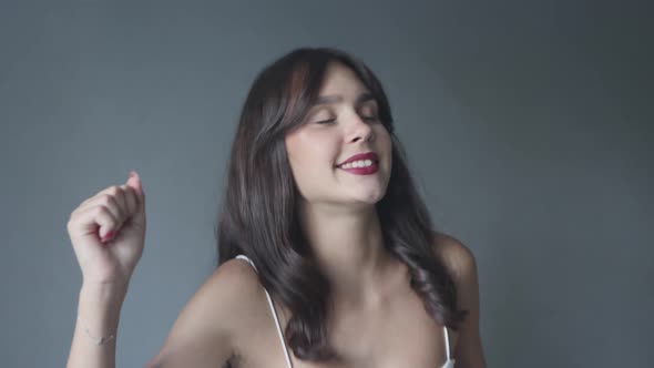 Pretty Young Female Brunette in White Shirt Dancing Enjoying on Grey Background