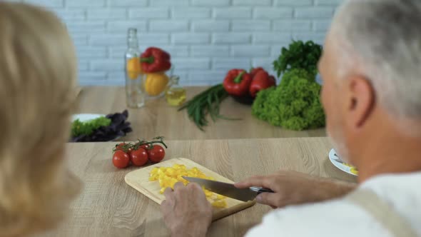 Husband Cutting Vegetables and Looking at Wife With Love, Married Couple Cooking