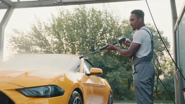 Handsome African Young Man in Protective Overalls Washing His Yellow Car