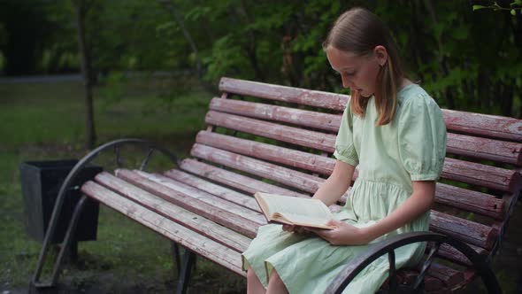 Girl Sitting on Wooden Bench and Reading Book Outdoors