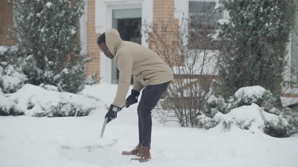 Wide Shot of Young African American Man Cleaning Snow Under Snowfall Outdoors