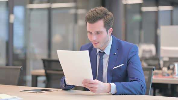Businessman Celebrating Success While Reading Documents in Office