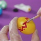 A man's hand, wearing a transparent glove, draws red dots on a Easter egg on a purple table. - VideoHive Item for Sale