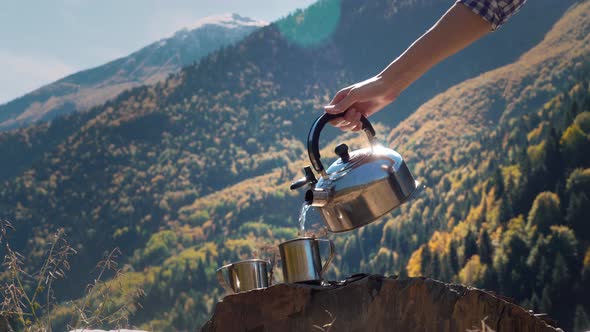 20    female traveler pours hot water from kettle into metal mug in close-up,