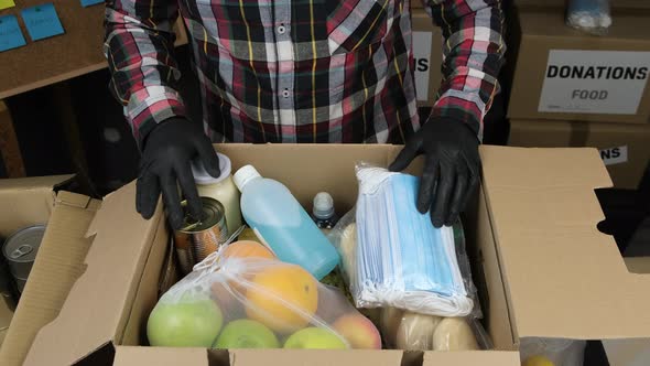 Incognito Volunteer in gloves put in box sanitizer and face masks and close Donation cardboard 