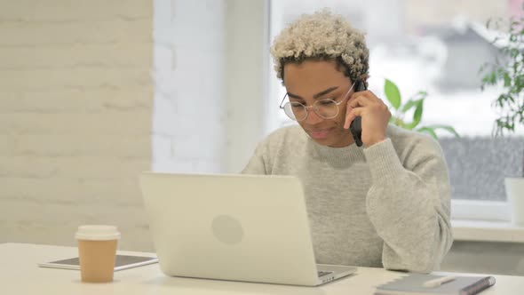 African Woman Talking on Smartphone While Using Laptop in Office