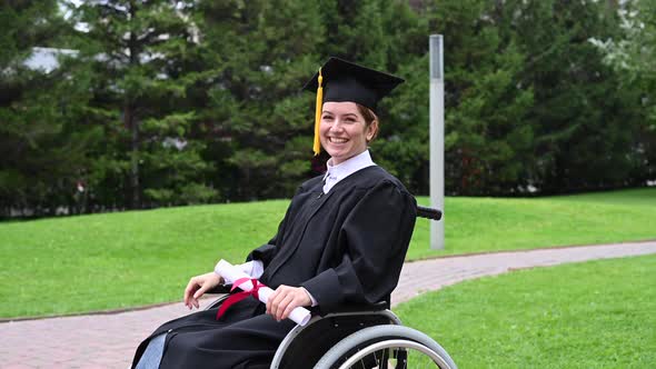 Caucasian Woman in a Wheelchair in a Graduate Costume Rejoices at Receiving a Diploma