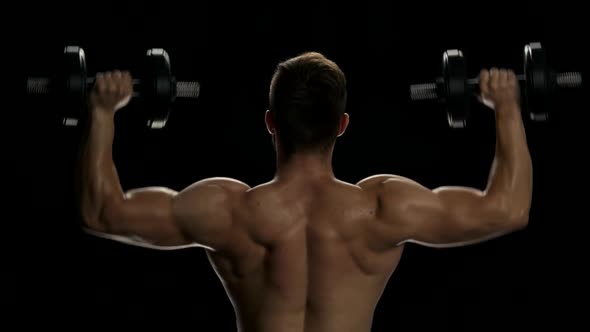 Rear View Muscular Man Lifting Dumbbells.