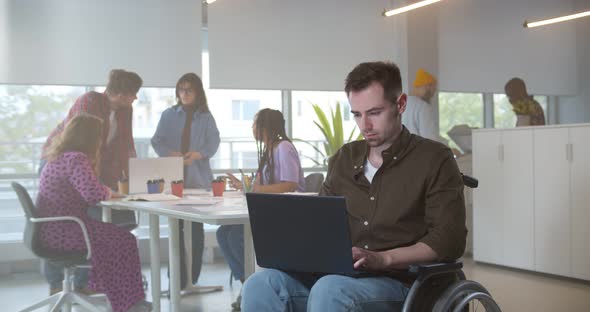 Disabled Young Man in Wheelchair Working in on Laptop in Modern Office