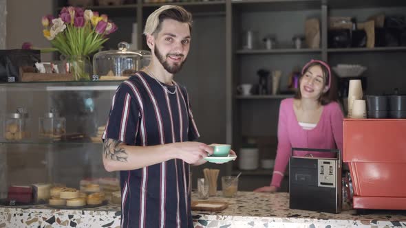 Tattooed Bearded Male Client Taking Coffee Cup From Female Barista in Vintage Coffee Chop Looking at