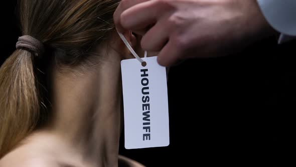 Male Hand Hanging Housewife Label on Female Ear, Outdated Woman Role in Society