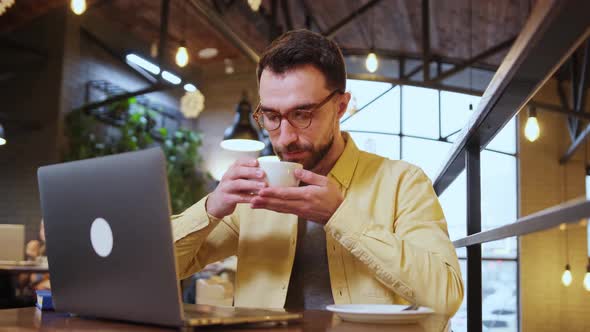 Young Man Enjoying with Drink Coffee Tea or Chocolate While Working with Laptop