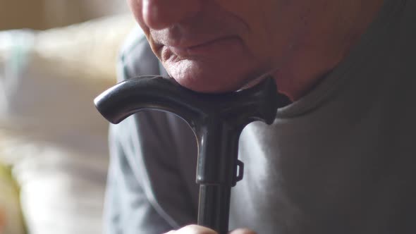 Portrait of an elderly Caucasian man 70-80 years old leaning his head on a cane stick for walking. A