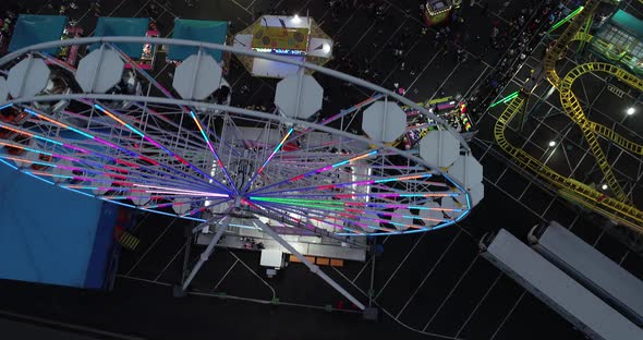 Aerial birds eye view of carnival/fair. Dolly forward over ferris wheel at night.