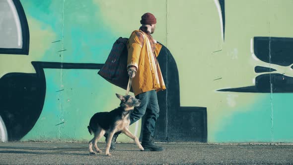 A Beggar with His Dog are Passing By a Graffiti Wall