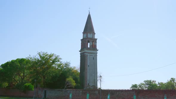 Church Bell Tower with Brick Fence Stands Among Trees