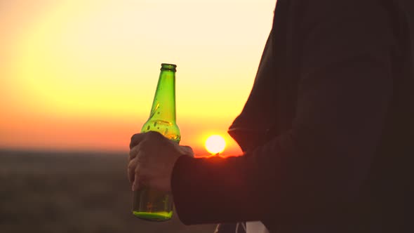 Close Up of a Man Drinking Beer at Sunset Standing on the Roof of a Building Against the Background