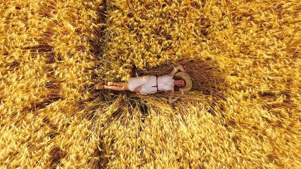 Young Woman Lying among Ripe Wheat Ears in Golden Wheat Field
