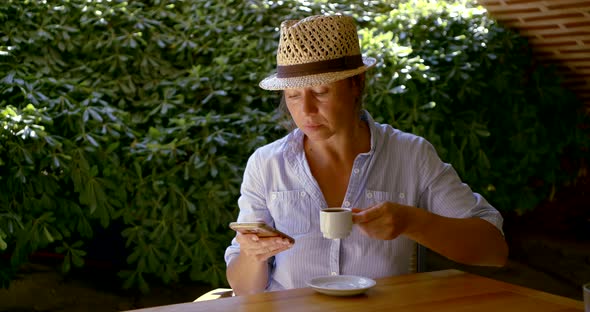 Female Tourist Is Resting in Cafe in Open Terrace, Drinking Coffee and Watching in Smartphone