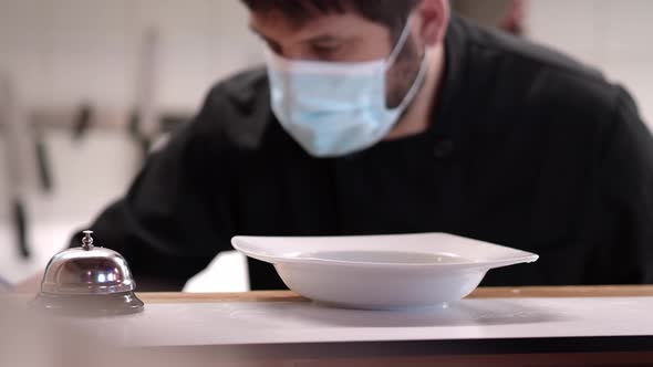 Chef with Medical Mask Serving a Dish in a Restaurant