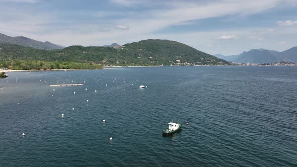 Low aerial orbit of a boat anchored on a giant mountain lake with buoys tree covered hills, distant