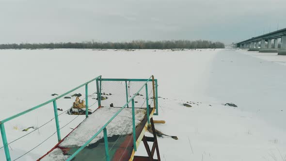 Rusty Pier Stands in Frozen River with Fallen Tree in Snow