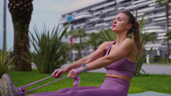 Sporty Woman is Training Alone in Park at Morning Using Elastic Tape