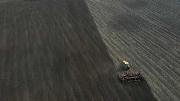 Aerial view of a modern yellow tractor plowing dry agricultural field, preparing land for sowing