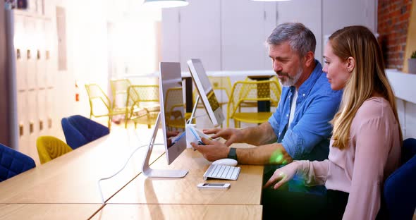 Business executives using digital tablet while disusing over computer