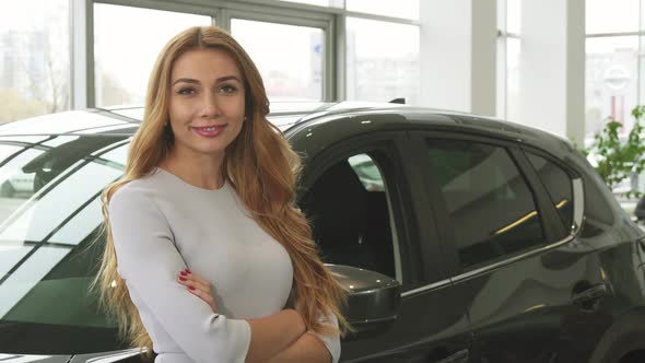 Young Beautiful Woman Smiling To the Camera Standing at the Car Dealership