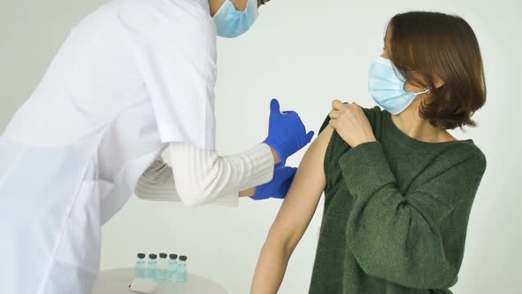 Female Doctor or Nurse is Giving a Shot or Vaccine to a Patient's Shoulder of Young Woman in Green