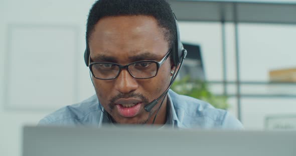 Portrait of African Man in Glasses Working Online Video Conference Using a Laptop with Headset at
