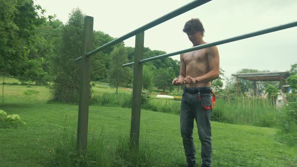 Young fit topless man stretches wrists before jumping to parallel bars