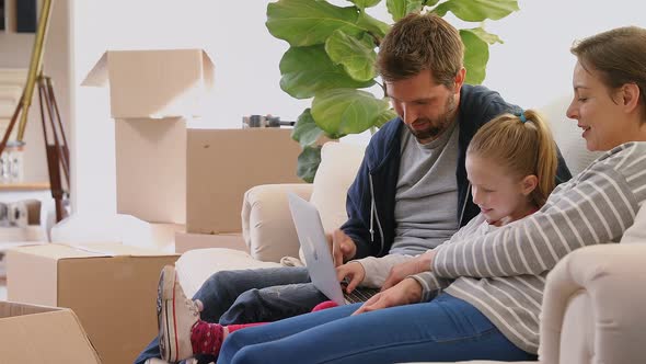 Family sitting on sofa and using a laptop in their new home 4K