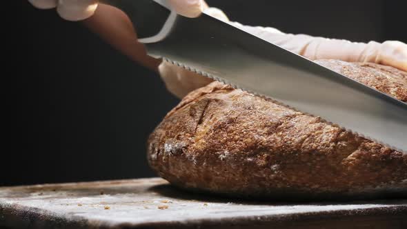 Chef in Gloves Cuts Lump of Tasty Rye Bread Loaf on Board
