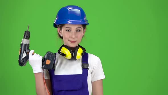 Engineer Girl in a Helmet and Overalls Holds a Drill in Her Hands . Green Screen. Slow Motion. Close