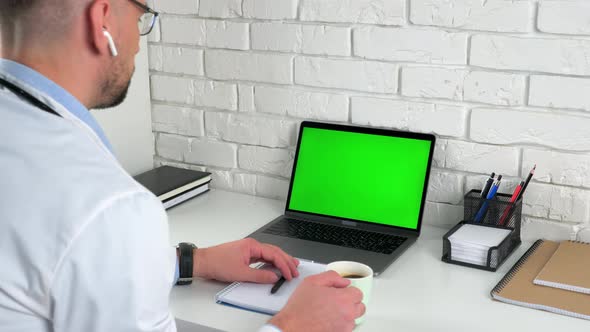 Doctor looking green screen laptop computer listens patient drinking coffee tea