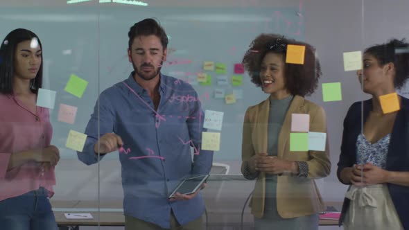 Diverse colleagues using memo notes and drawing on glass wall having a discussion