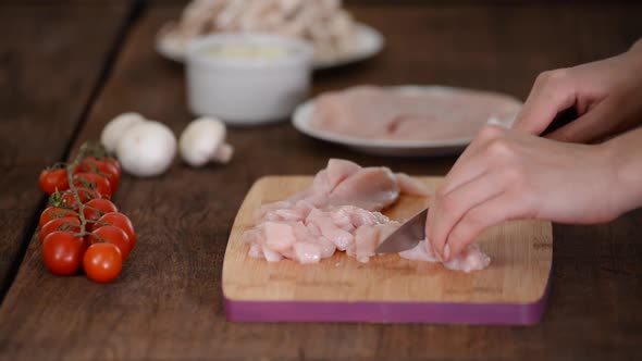 Female Hands Cutting Chicken Fillet on Wooden Chopping Board.