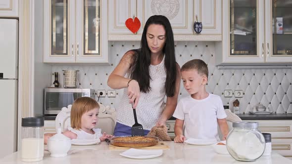 Mother and Two Kids Cutting Raspberry Pie in Kitchen