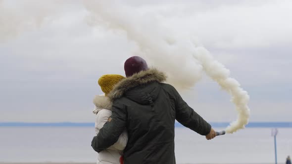 A Couple in an Embrace on the Shore Let Out Colored Smoke