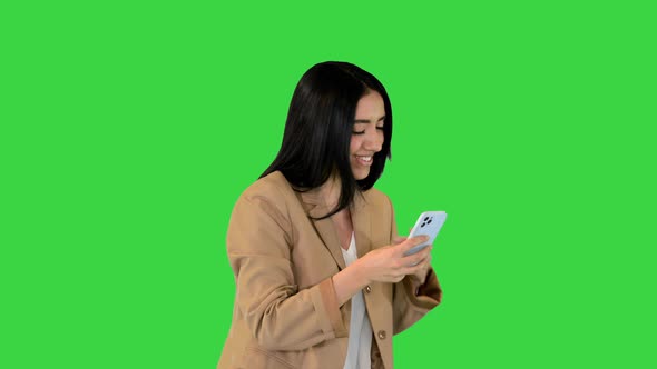 Young Indian Girl Walks and Smiles with Mobile Phone in Hands on a Green Screen Chroma Key