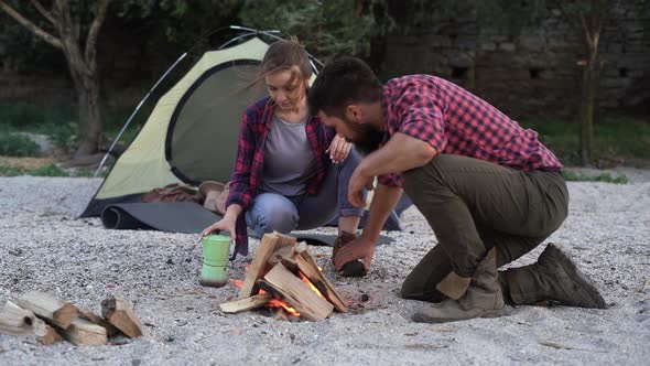 Married Couple Prepares Food on a Campfire on Shore of Lake with a Tent