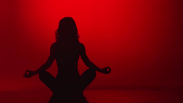 Silhouette of Relaxed Woman Meditating Sitting in Lotus Position on Red