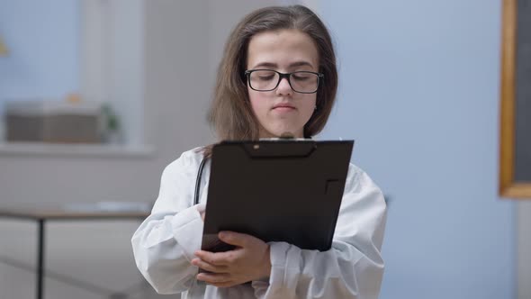 Front View Caucasian Woman Physician with Paperwork Putting Down Eyeglasses Looking at Camera with